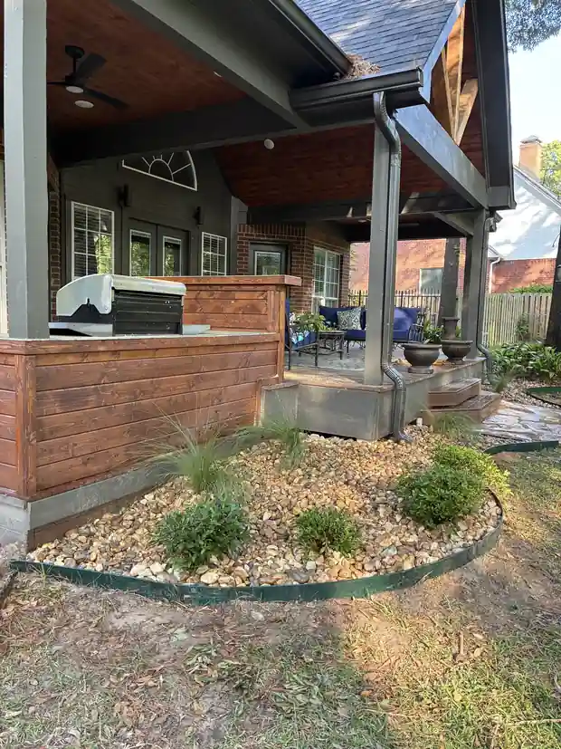 River rock bed with grasses and steel edging wrapping a cedar outdoor kitchen under a covered patio