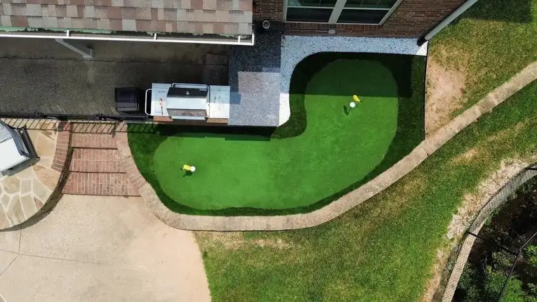 Drone view of a kidney-shaped artificial turf putting green beside a house