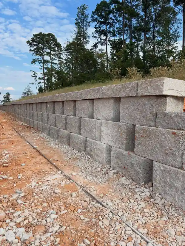 Long grey segmental block retaining wall on red East Texas clay with pines above