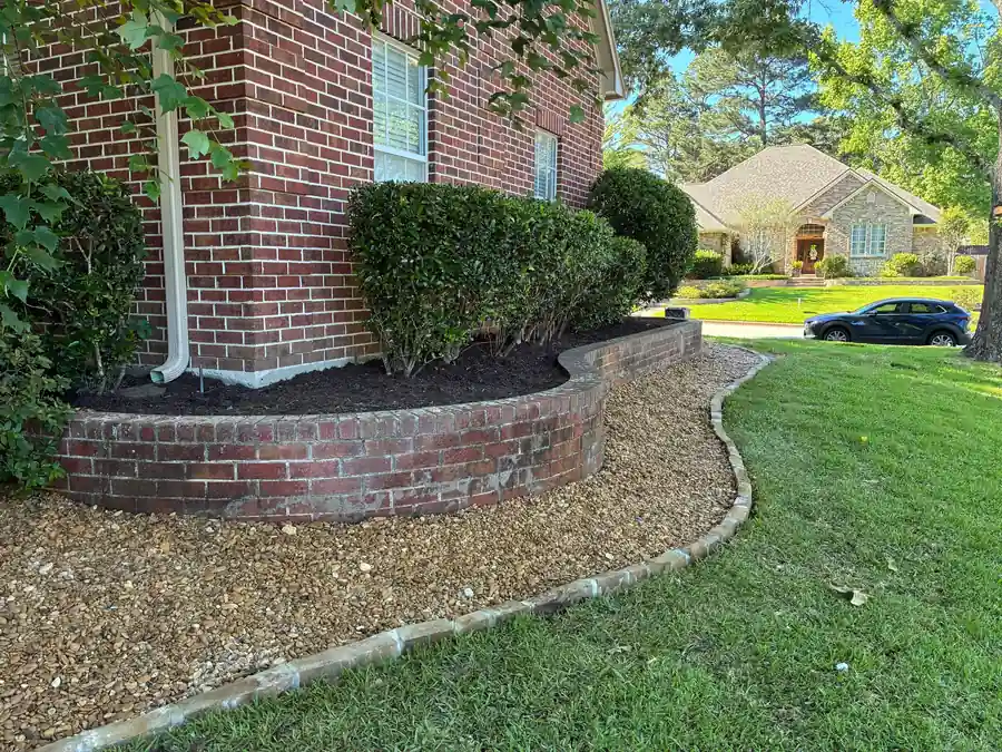 Hollytree, Tyler: a raised brick bed with brown hardwood mulch, a run of river rock and a mortared stone border curving into St. Augustine lawn